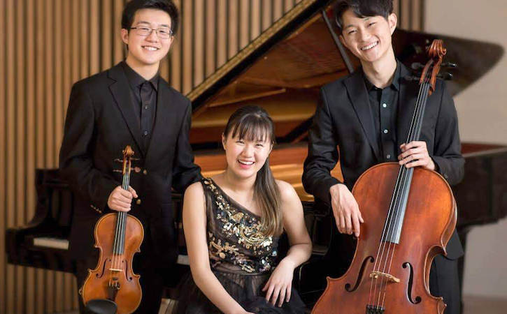 Bach Trio holding their instruments in front of a piano