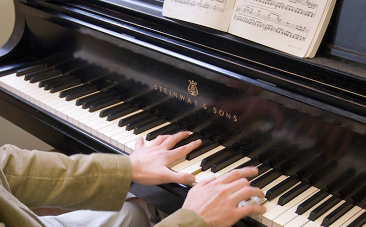 Piano with sheet music and keys being played by two hands