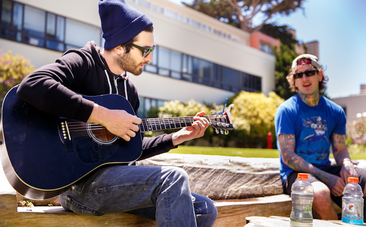 Two men outside, one playing the guitar