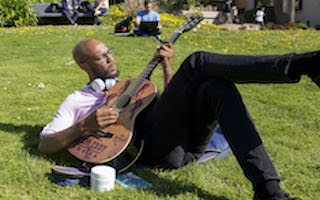 Man playing guitar out on the grass on campus