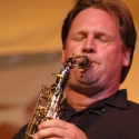 Andrew Speight, a white man in a black polo shirt, playing his saxophone. His eyes are closed and his hair pushed back from his forehead.