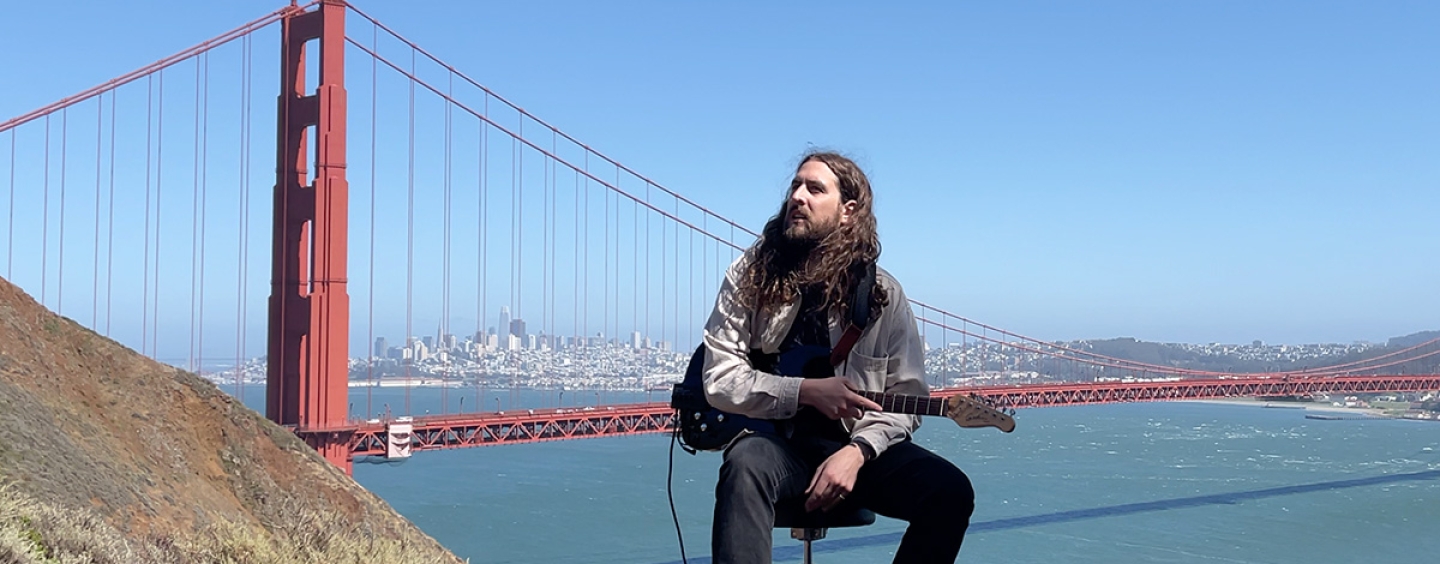 Nate Mercereau seated outdoors in the Marin Headlands holding a guitar