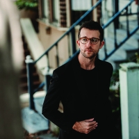 Chad Goodman a young white man with short brown hair and glasses walking down a city street and looking at the camera